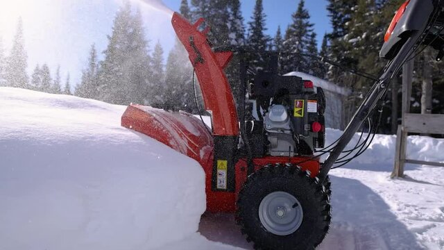 Close up shooting of a bright orange mechanical snowplough being pushed straight against a heap of fresh snow recently fallen by a young man.