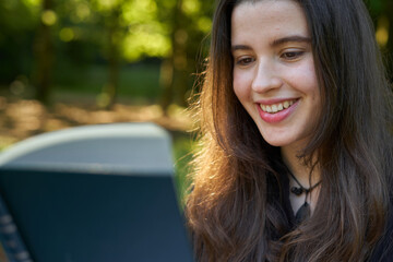 beautiful long-haired woman reading a green book in nature sitting on the grass with a blanket and her bag with trees in the background. teenager looking at a literary work in the park smiling