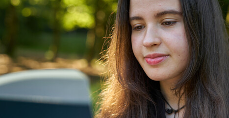 beautiful long-haired woman reading a green book in nature sitting on the grass with a blanket and her bag with trees in the background. teenager looking at a literary work in the park smiling