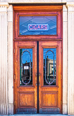 Vertical vintage double wooden doors  with transom window with CIGAR sign hanging and old fashioned...