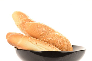 Several fragrant bagels sprinkled with sesame seeds in a black ceramic plate, close-up, isolated on white.