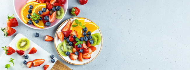Web banner with fresh summer salad of various fruits and berries. Kiwi, orange, strawberry and blueberry on a plate decorated with mint on a table top view, free space for text