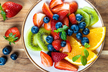 Fresh summer salad of various fruits and berries. Kiwi, orange, strawberry and blueberry on a plate decorated with mint on a blue wooden rustic background top view