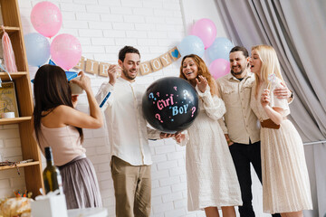 Excited couple blowing up surprise balloon during gender reveal party - obrazy, fototapety, plakaty