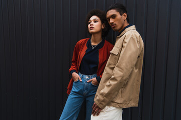 young african american man looking at camera while posing with curly woman in jeans outside