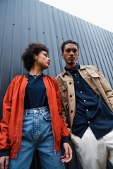 low angle view of african american couple in trendy jackets posing outside