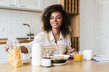 The happy woman taking a package of cereal while sitting at the table in the kitchen