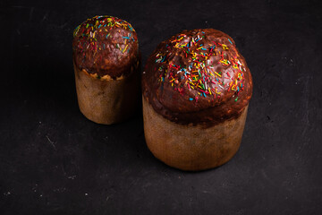 Two Easter cakes, sprinkled with chocolate and sprinkled with sweets, stand on a black background in the photo studio.