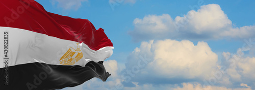 Large flag of Egypt  waving in the wind on flagpole against the sky with clouds on sunny day. 3d illustration