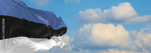 Large flag of Estonia  waving in the wind on flagpole against the sky with clouds on sunny day. 3d illustration