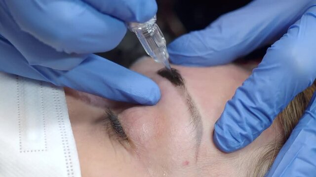 Eyebrow microblading is done with a motor with a blade . High quality 4k footage.The beautician has hands in blue gloves