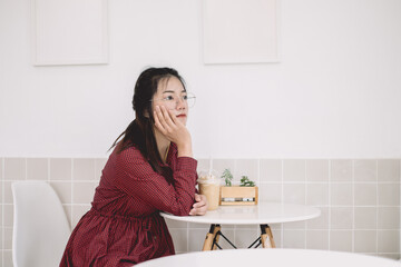 Asian girl teen sitting thinking day dream boring and thoughtful look away in white cafe alone.