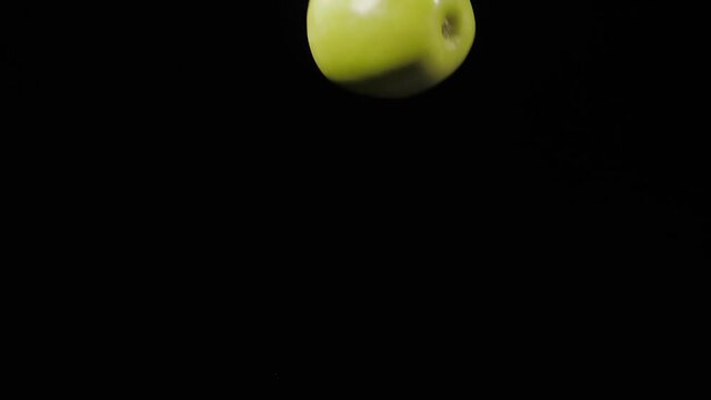 Close up on the three fresh juicy green apples fly up and spinning on a black background in slow motion shot