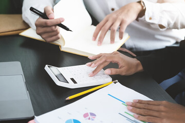 Two young business executives are discussing to change their business concept to increase profits and the strength of their business with using calculator and laptop for work.