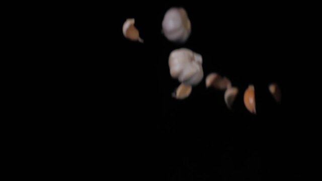 Close up on the garlic and garlic cloves tossed up in the air and spinning on a black background in slow motion shot