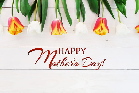 Composition of spring flowers on wooden background. White and red with yellow tulips. Inscription Happy Mother's Day. Advertising content for Mother's Day. Flat lay, top view, close up, copy space