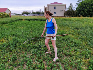 Young woman mows the grass scythe in the countryside