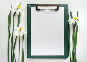 Green clipboard with daffodils on white background, home office workspace flat lay.