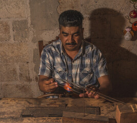 Craftsman blowing glass to create Christmas balls in his workshop, with the help of a blowtorch he shapes the glass tubes to turn them into spheres of different shapes.