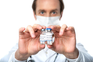 Jars with coronavirus lettering on vaccine in hands of blurred doctor isolated on white
