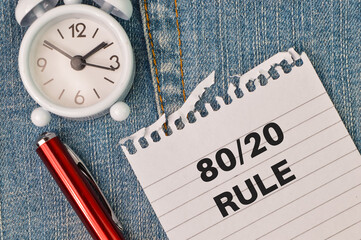 Phrase 80/20 RULE written on white paper with pen and clock. Business concept.