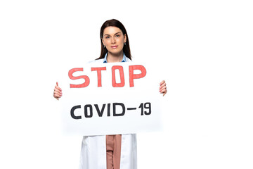 Brunette doctor in white coat holding placard with stop covid-2019 lettering isolated on white