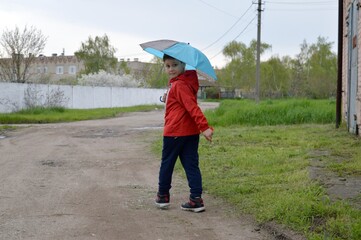 A boy in a red jacket and carrying an umbrella walks on a spring, rainy day with his family.