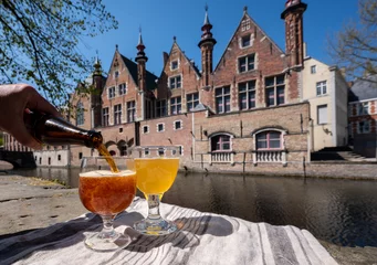 Fotobehang Proeverij van Belgisch bier op open café of bistroterras met zicht op middeleeuwse huizen en grachten in Brugge, België © barmalini