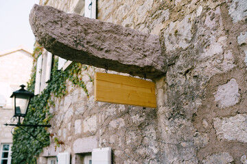 Empty wooden signboard on a stone pin of an old building amid windows, lantern and greenery