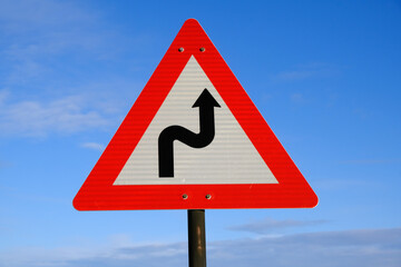 Road warning sign twisting road against a blue sky