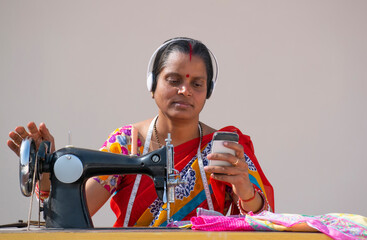 PORTRAIT OF A RURAL WOMAN listening music AND SEWING CLOTHES holding mobile	 - obrazy, fototapety, plakaty