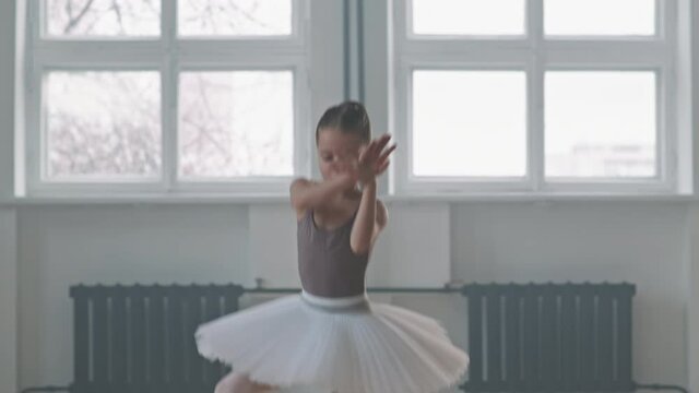 Medium tracking shot of talented 9-year-old ballerina in tutu dancing alone in spacious loft-style dance class