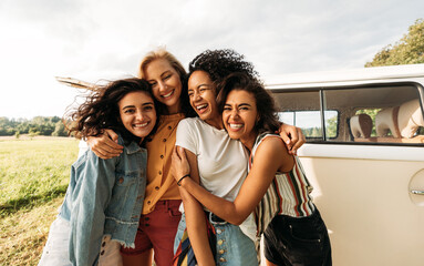 Four happy female friends laughing together standing in front of a van. Women enjoying summer road trip. - obrazy, fototapety, plakaty