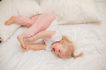 Cute little blonde girl lies at home in bed with white linen, view from above