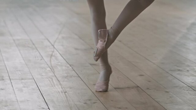 Low-section shot of little ballerinas legs in pointe shoes dancing ballet on wooden floor in dance studio