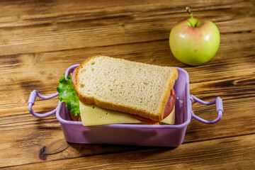 Lunch box with sandwiches and apple on a wooden table