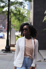 Gorgeous woman walking down the street with sunglasses. close up portrait, african american model, natural hairstyle, purse on shoulder, casual blazer fashion, one person, background