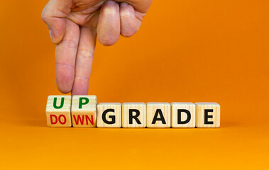 Upgrade or downgrade symbol. Businessman turns wooden cubes, changes words 'downgrade' to 'upgrade'. Beautiful orange table, orange background, copy space. Business and upgrade or downgrade concept.