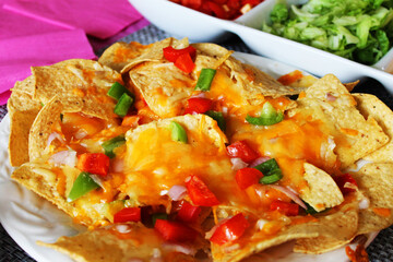 Close-up of a table set for a party, with nachos, a dish of taco toppings, a pink table cloth and napkins, place mats and paper plates.