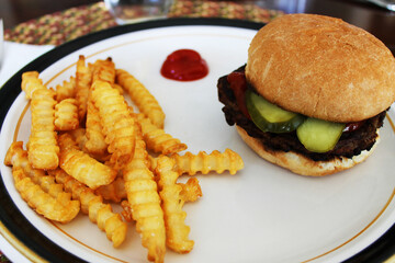 Close-up of a hamburger and French fries on a plate, with a dollop of ketchup.
