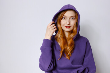 A redhead woman in a purple hoodie adjusts the hood. White background - Powered by Adobe