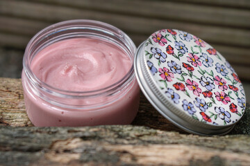  Pink face cream or body cream in packaging with flowers on a dark background. Rose face cream. Rose hip cosmetics. Homemade face cream. 