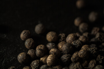 Close up of group of dried peppercorns in lower right corner on slate plate