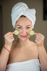 women with mask for face lie with towel on head and has cucumber on face