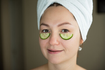 women with mask for face lie with towel on head and has cucumber on face