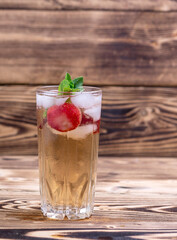 a glass of iced tea with strawberries and mint on a wooden background. soft drinks in the heat
