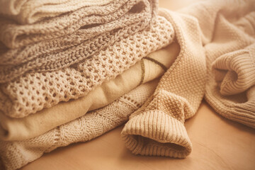 Warm knitted white wool sweaters are stacked in a pile, illuminated by the sunlight. Autumn. Cold weather clothing. Home comfort.