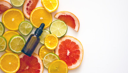 Natural cosmetics with vitamin C, a bottle with a cosmetic product with citrus essential oil on the background of plastics of lemons, oranges, grapefruit. Copy space. Citrus skin whitening concept