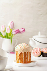 Easter cakes Kulich, tulips and white utensils for a tea ceremony on a bright background. Holiday concept