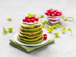 Fototapeta na wymiar Spinach pancakes with cream and cranberries on a plate on a light gray background